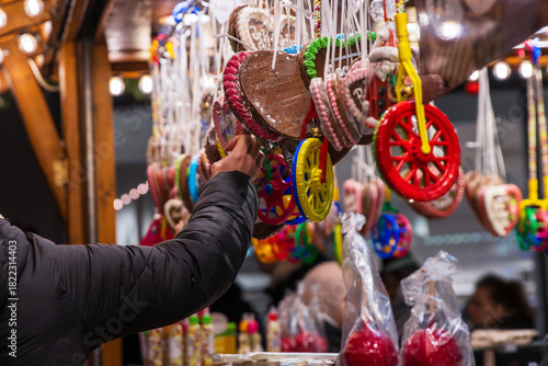 Customer’s hand selecting an item at a vibrant display of colorful candy wheels, gingerbread hearts, and festive sweets at a traditional christmas market stall
