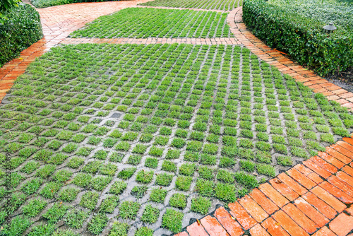 Sustainable landscaping design featuring a permeable concrete paver system with grass growing through the grids, bordered by red clay bricks.
