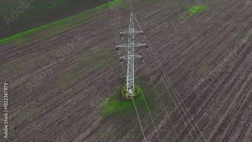 Aerial drone view of power transmission lines stretching across open terrain, tall pylons and cables forming strong linear patterns that highlight energy distribution and industrial landscape.