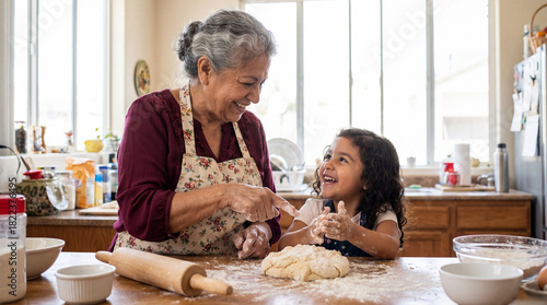 A happy elderly Hispanic woman and her granddaughter laugh while playing with flour and kneading dough on a wooden kitchen table, enjoying baking together.