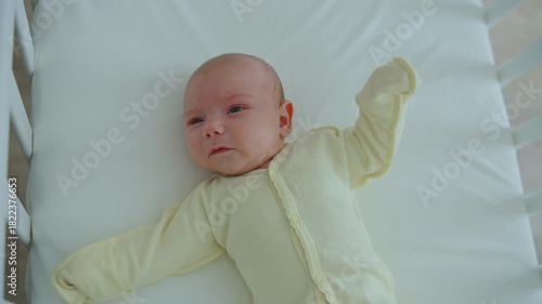 A one-month-old baby lies in a wooden crib, kicking and crying