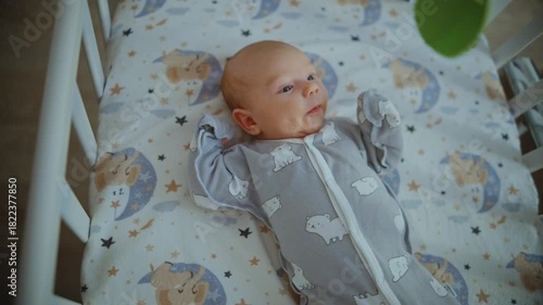 An infant lies in a crib and looks at a mobile that spins above its bed