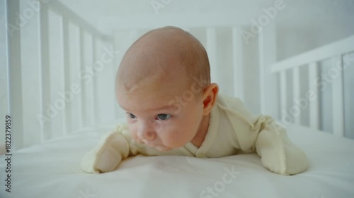 A small one-month-old baby is lying on its stomach in a crib and trying to lift its head. The concept of children's development