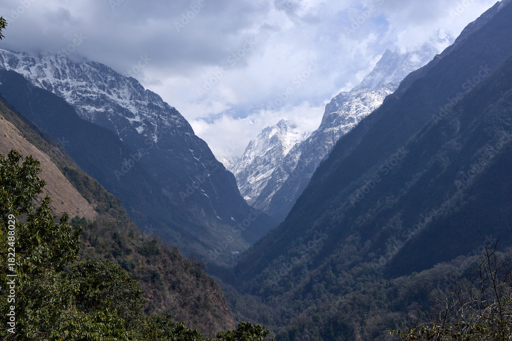 Fototapeta premium A view of the valley on the route to Annapurna Base Camp in Nepal. The Himalayas are visible, showcasing snowy peaks and dense forests along the trekking path
