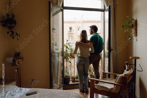 A man and a woman are standing at the entrance to a balcony and he is hugging her