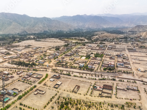 Aerial panoramic view of urban expansion in the Cieneguilla valley near Lima Peru showing residential neighborhoods and green areas surrounded by arid mountains.