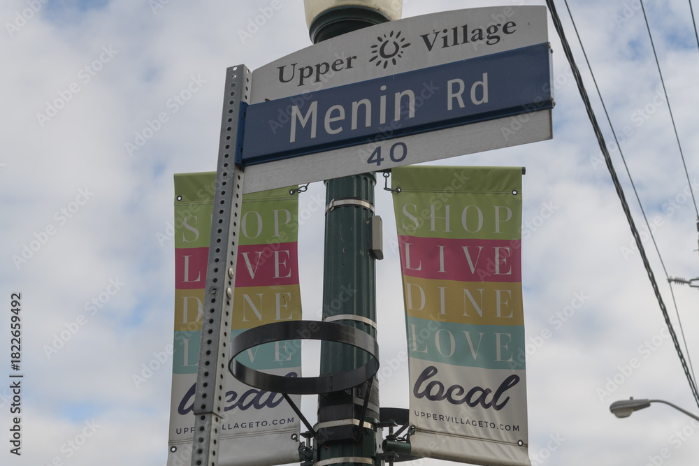 Fototapeta premium street sign at Upper Village (Menin Rd) and BIA promotional banners, Eglinton Av W, Toronto