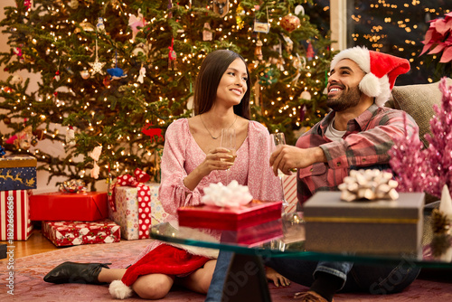 Happy couple celebrating Christmas morning together with champagne and gifts by decorated tree