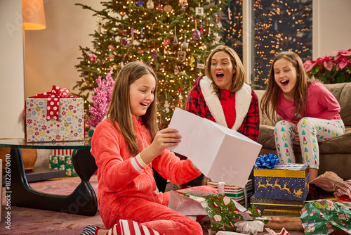Mother and daughters enjoying Christmas morning gift opening in festive pajamas by decorated tree