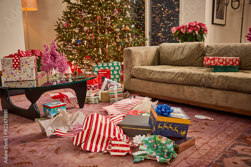 Festive living room with illuminated Christmas tree and unwrapped presents scattered across the floor