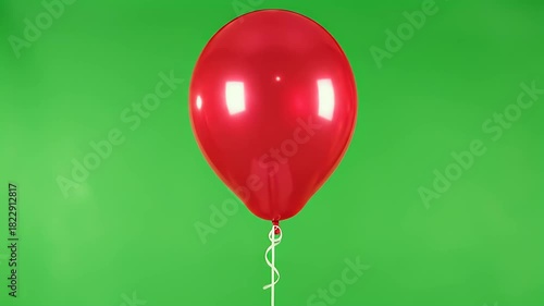 A red balloon floating against a green background, captured from a straight-on viewpoint.