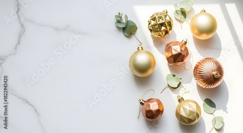 Elegant Christmas flat lay with gold and copper baubles and eucalyptus leaves on white marble background with sunlight and copy space
