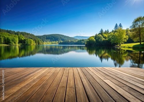 A wooden deck overlooking a serene lake on a clear blue sky with trees and hills in the background