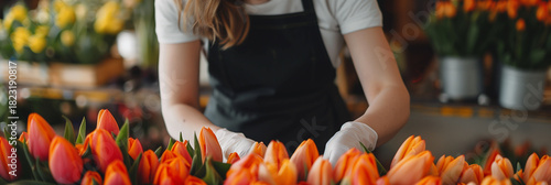 A skilled florist delicately collects fresh orange tulips in spring, dressed in an apron and white gloves. The soft focus of a warmly lit floral shop creates a welcoming atmosphere.