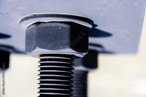 Large industrial bolt secured with a nut to a metal plate. Details of the threads and the sturdy construction