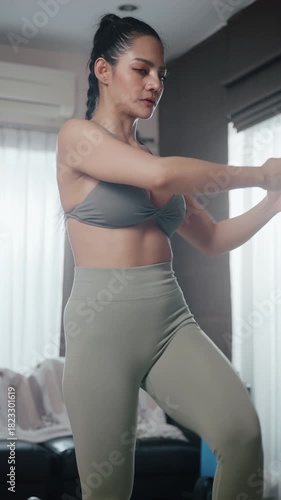 Vertical clip. Attractive Asian woman in sportswear exercising at home.