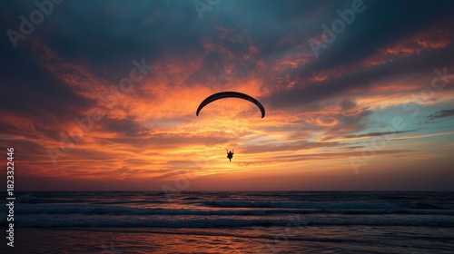 Paraglider silhouetted against a vibrant sunset over the ocean