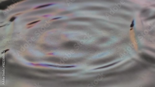 Shimmering slow-motion surface texture of iridescent silver fluid creates gentle concentric resonant ripples moving outward meditative, metallic sheen, fluid motion