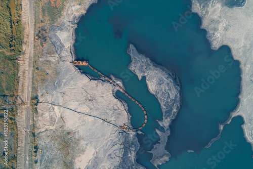 Aerial drone shot of a large industrial tailing pond (slurry storage) showing a dredge and pipeline actively moving industrial waste. Environmental contamination and industrial pollution.