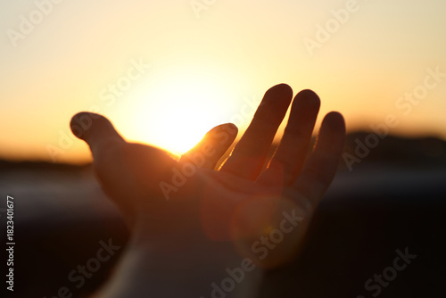 Obraz na płótnie A hand reaching out toward the brightly rising sun, a New Year's sunrise background filled with hope for a brighter tomorrow and hopes and aspirations