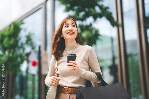 Single beautiful adult asian business woman holding take away coffee cup and black shopping bag