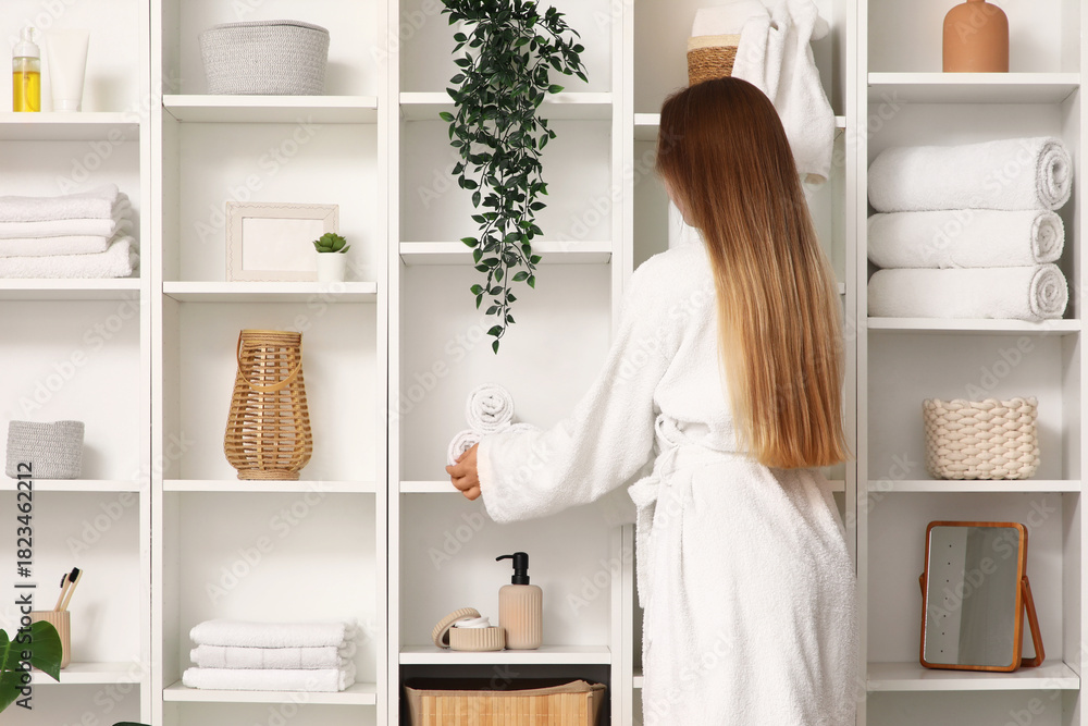 Obraz premium Young woman with towels on shelf unit in bathroom, back view