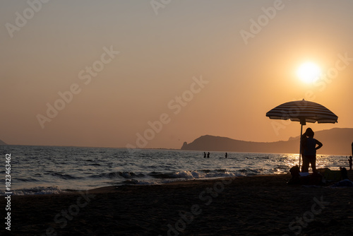 Fototapeta Naklejka Na Ścianę i Meble -  Silhouettes of swimming people on sunset in sun lights, sandy beach near Sperlonga, Lazio, italy, summer vacation