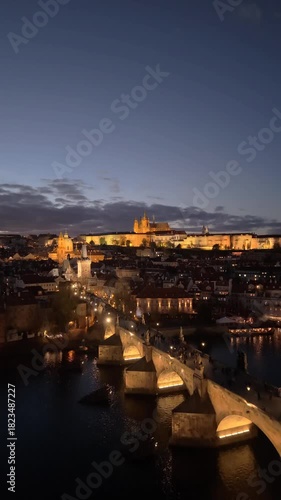 Experience the beauty of Prague at dusk with aerial views of the historic Prague Castle and illuminated Charles Bridge over the Vltava River, showcasing a vibrant cityscape.