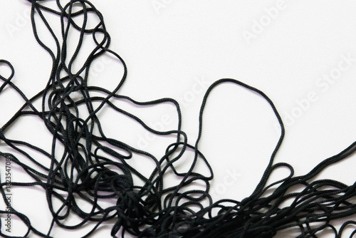 A cluster of thin black cords lies in a loose, chaotic tangle against a clean white background