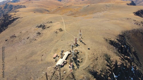 Aerial view of a remote telecommunication relay station featuring multiple towers and buildings situated on a high, barren mountain ridge
