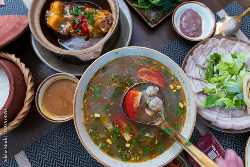Refreshing sour clam soup with tomatoes and herbs, served alongside braised fish and boiled pork in a traditional Hue meal.