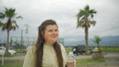 Woman drinking water from a bottle after sports with palm trees
