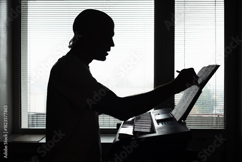 Silhouette of male pianist playing musical instrument at home. Silhouette of a man writing music notes while composing at keyboard