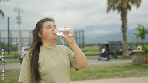 Woman drinking water from a bottle after sports with palm trees slowmotion