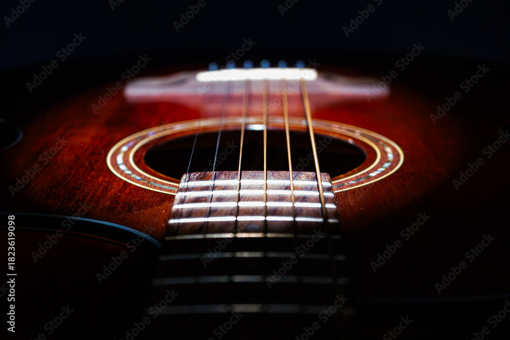 Obraz premium Close-up of a vintage wooden acoustic guitar against dark backdrop, strings running vertically, headstock with tuning pegs, warm lighting, slight angle view focusing on textured details