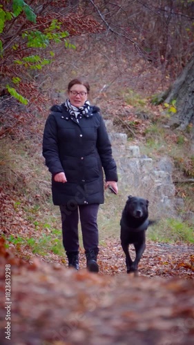 Woman Walking a Black Dog on an Autumn Forest Path
