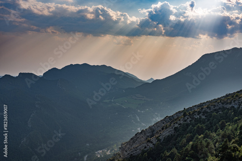 Dramatic sunset landscape over the mountains of Berga, Catalonia, Spain, featuring intense crepuscular sun rays piercing through clouds and highlighting the valley below.
