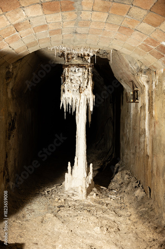 Mineral discharge chute covered in white stalactites (artificial speleothems) and rust, inside a dark, humid tunnel of the abandoned Asland cement factory.