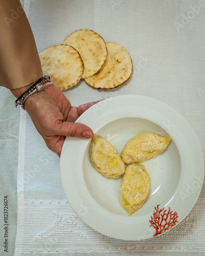 A person holding a porcelain plate containing homemade pasta called culurgiones