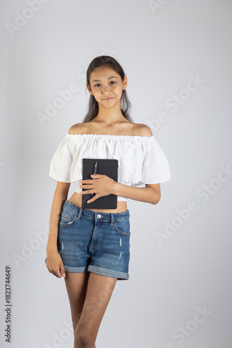 A young woman is standing and holding a book or tablet in her hands