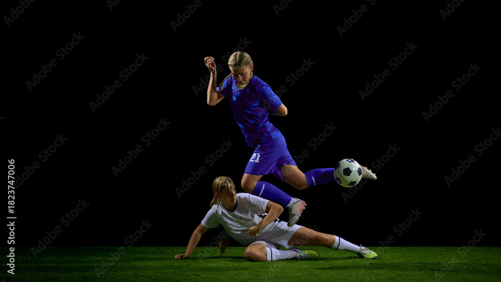 Fototapeta premium Teenage female soccer players in sliding tackle duel during active play. Concept of youth defensive training, contact-technique instruction, tactical coaching, match analysis.