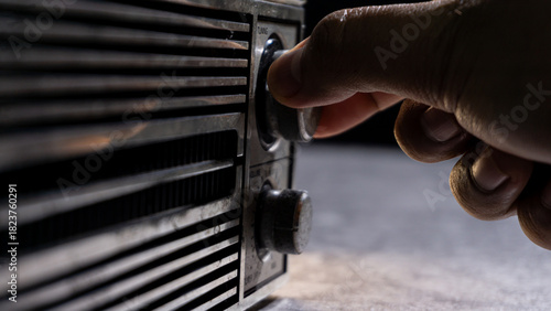 Schilderij op canvas A hand adjusting the tuning knob of a weathered radio, with dramatic shadows highlighting texture and vintage craftsmanship