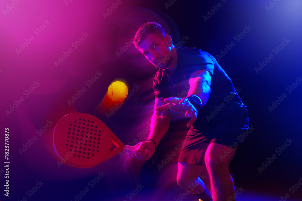 Fototapeta premium Man playing padel tennis under colorful lights in a dimly lit environment