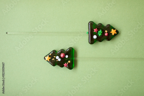 Two green christmas tree shaped lollipops arranged horizontally on a muted green background with clean lines and ample copy space