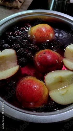 Apples and blackberries are boiled in water in a saucepan to make compote