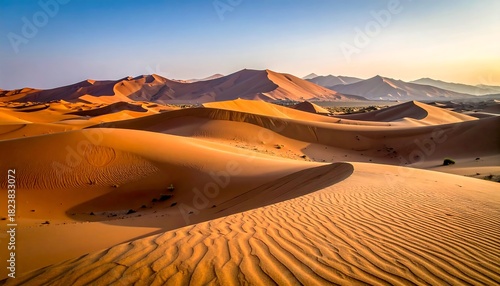 Fototapeta Naklejka Na Ścianę i Meble -  Golden sand dunes stretch under a bright blue sky, with distant mountains visible on the horizon at dawn