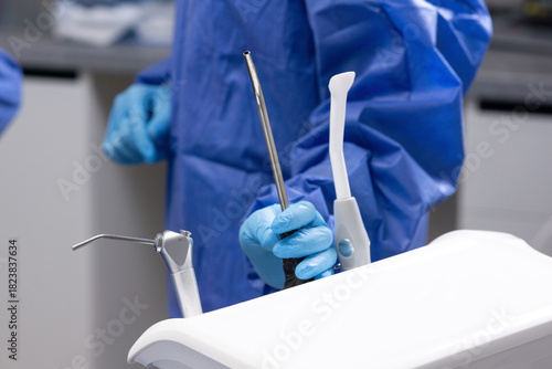 Medical theme, female hands wearing gloves and a surgical gown, holding a saliva ejector, dentistry.