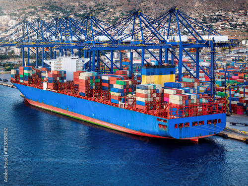 Aerial view of  a container super cargo ship being unloaded and loaded by cranes and trucks in a commercial terminal