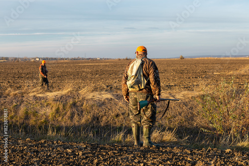 Mature man hunter with gun while walking on field.