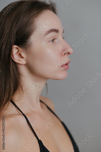 Profile view of a young woman with long hair standing against a neutral backdrop